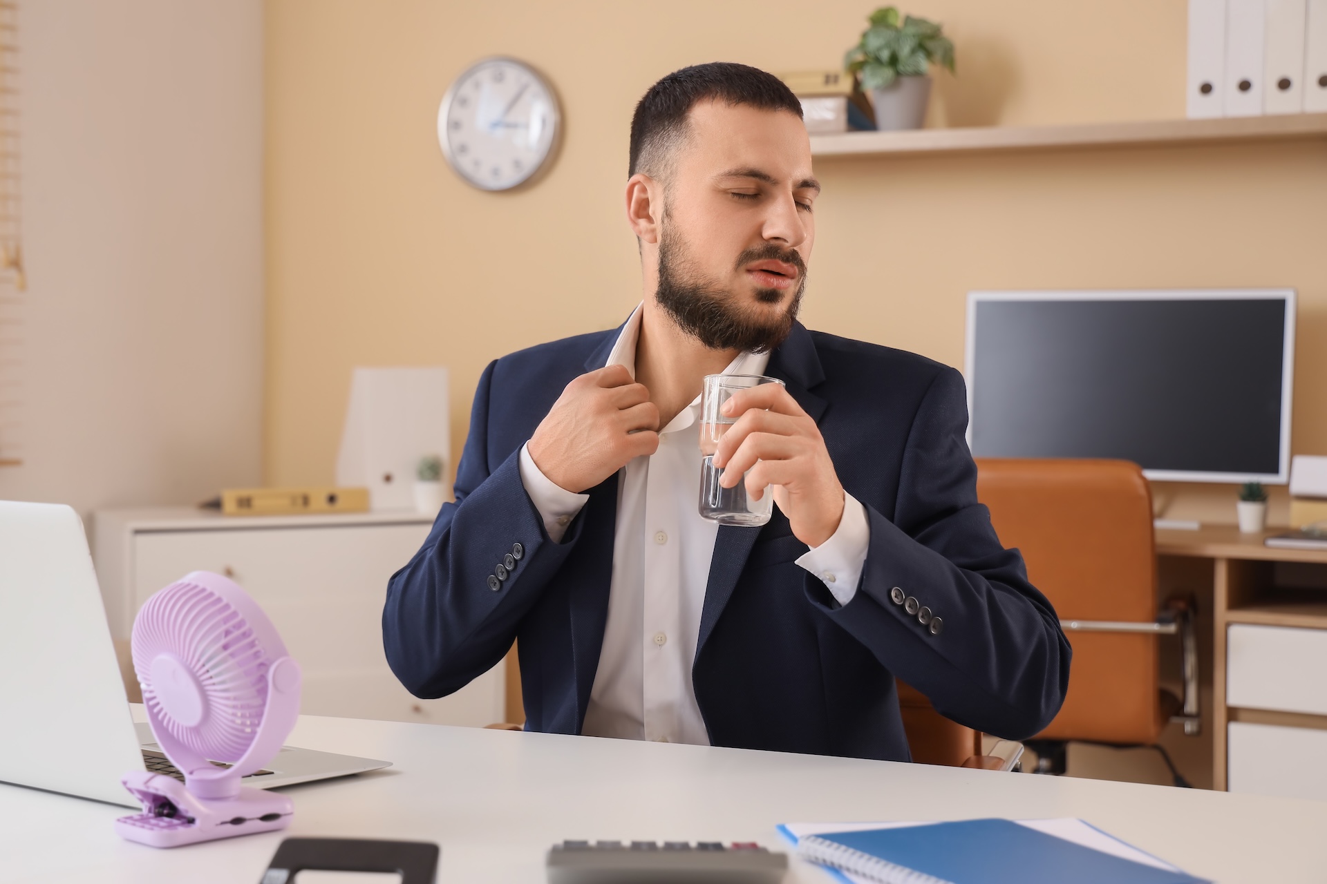 Zaměstnanec v kanceláři v horkém létě s ventilátorem